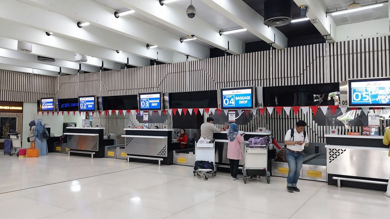 A bright airport check-in hall with travellers and luggage moving past the counters
